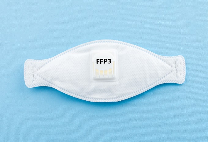 Eine FFP3 Maske liegend vor einem hellblauen Hintergrund