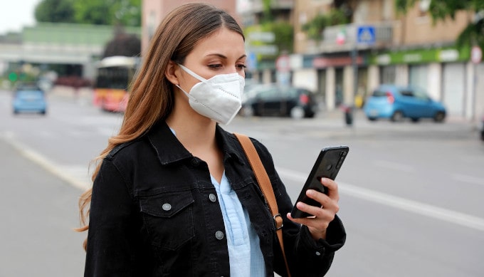 Junge Frau trägt eine FFP2 Maske und guckt dabei auf Ihr Handy